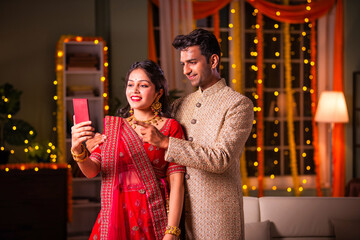 Indian young couple celebrating diwali and taking selfie using smartphone at home