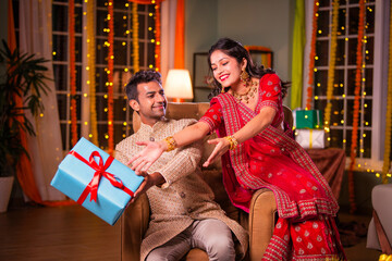 Playful Indian young couple celebrating diwali with gifts, wife trying to get hold of present from husband