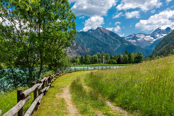 Narrow footpass along wooden fence and lake Brusson in Italy.