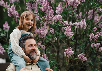 Dad having fun with young daughter, carry her on shoulders, walking in spring nature. Fatherhood and Father's Day.