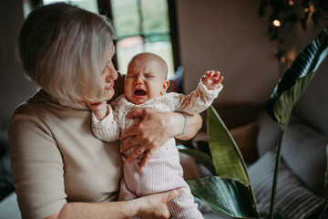 Grandmother holding crying baby girl in arms, calming her down, soothing her. Strong bond between...