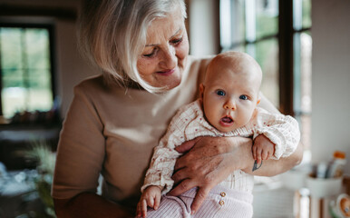 Lovely grandmother holding little baby in arms, looking at her lovingly. Strong bond between...