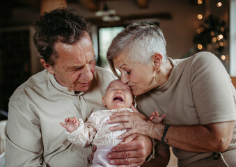 Grandparents holding crying baby girl, calming her down, soothing her. Strong bond between...