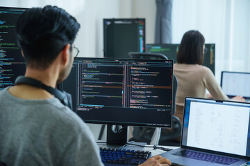 Asian software developers working on multiple screens displaying code and application diagrams in a...
