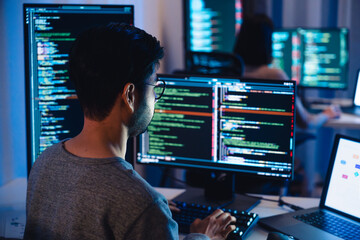 Asian software developers working on multiple screens displaying code and application diagrams at...