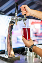 Hand pouring lemonade from a tap into a clear glass with blurred background