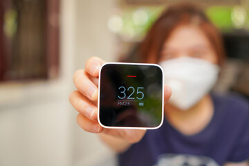 young asian woman hold PM2.5 detector indicate very high number of PM2.5 that harmful air quality to human health with selective focus on the device