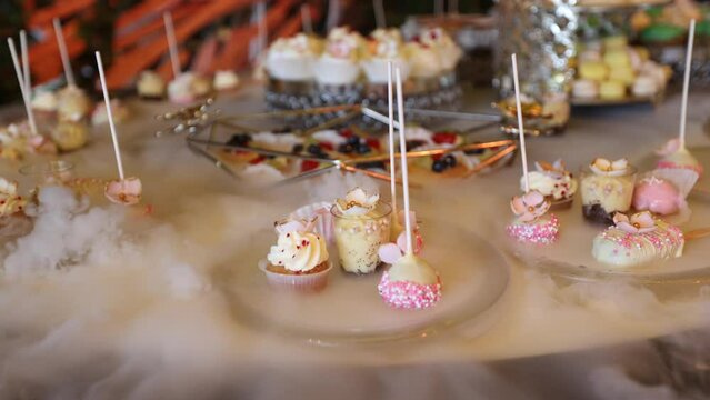 Luxury candy bar. 4K video with a premium elegant candy bar for weddings with plates of sweet floating on a carbonic ice water surface with smoke coming out between them.