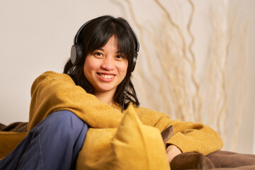 A woman wearing headphones and a yellow sweater is smiling