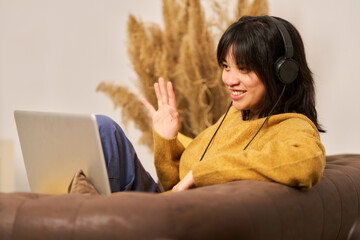 A woman wearing headphones is sitting on a couch and smiling
