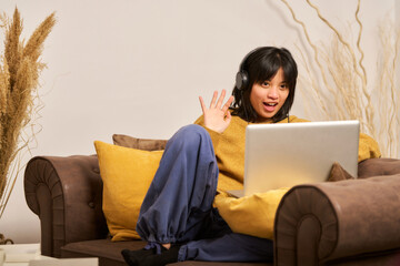 A woman wearing headphones is sitting on a couch with a laptop in front of her