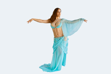 Beautiful young woman in stylish clothes dances tribal fusion oriental dances on an isolated light...
