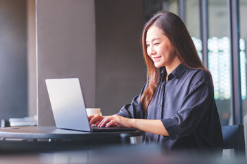 Portrait image of a young woman working and typing on laptop computer in cafe