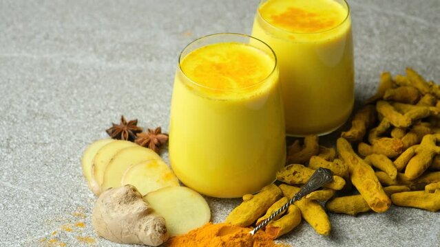 Golden milk, a traditional Ayurvedic drink with turmeric in two glasses on a gray background