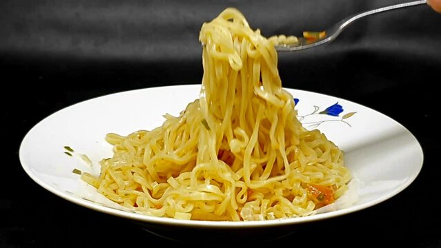 Instant noodles with fork, served with vegetables and herbs, on white plate