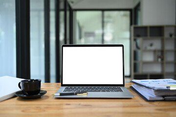 Front view laptop with empty display, documents and coffee cup on wooden office desk