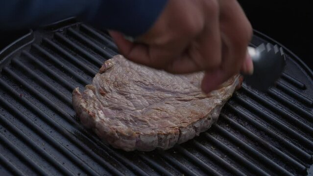 Close up of juicy beef steak flipped around with tongs on hot grill