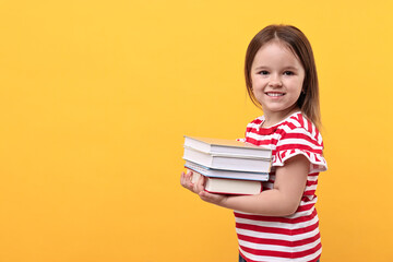 Cute little girl with books against orange background. Space for text