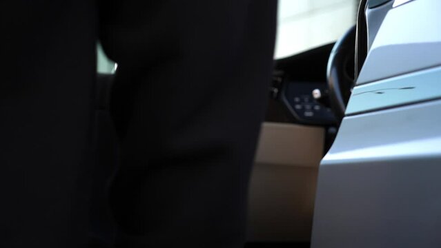 Male hand opening door and get in to modern car. Arm of man putting to button for opens door of automobile. Guy sits down into the auto. Concept of contemporary technologies. Close up Slow Motion