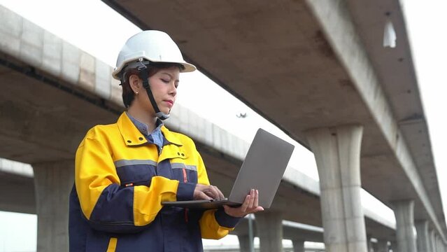 Asian female engineer uses laptop to inspect highway construction work