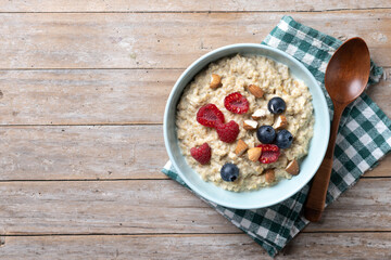 Oatmeal porridge with raspberries, blueberries and almonds in bowl on wooden table. Top view. Copy space