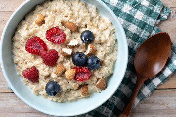 Oatmeal porridge with raspberries, blueberries and almonds in bowl on wooden table. Top view