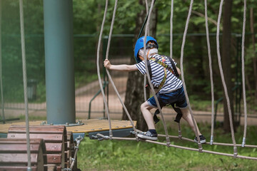 Summer. A small child climbs in a rope park on a rope bridge. A boy is having fun in an Adventure Park. A male baby on a climbing frame. Compliance with safety techniques.