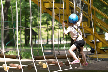 Summer. A small child is climbing a rope bridge in a rope park. A girl is having fun in an...