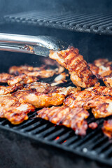 Close-up of marinated chicken meat grilling with smoke rising.