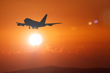 Airplane Silhouette Against Vibrant Orange Sunset Sky with Sun and Clouds in the Background,...