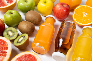 Assortment of fruit juices in glass bottles among fruits on white background top view