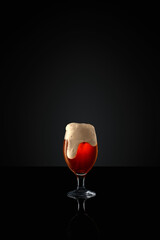 Glass goblet brimming with craft, dark beer, topped with thick, creamy foam against black studio...