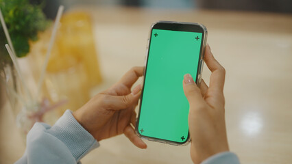 A woman uses a mobile phone or tablet with a green screen to watch videos, surf social media, or have an online conference.
