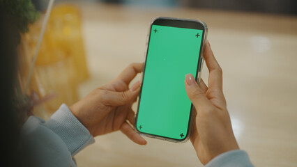A woman uses a mobile phone or tablet with a green screen to watch videos, surf social media, or have an online conference.