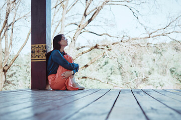 Teenage girl feeling lonely on wooden porch in traditional Asian setting. Outdoor candid emotional...