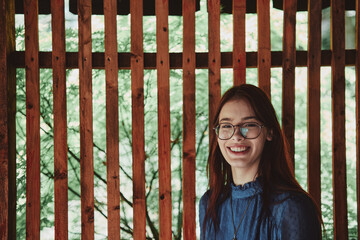 Happy teenage girl smiling in a wooden gazebo surrounded by lush greenery. Vibrant lifestyle...