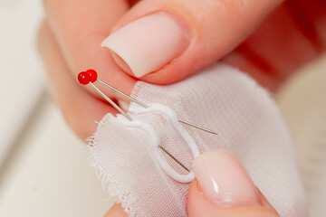 close-up of hands in sewing workshop hemming white fabric for a dress with a needle