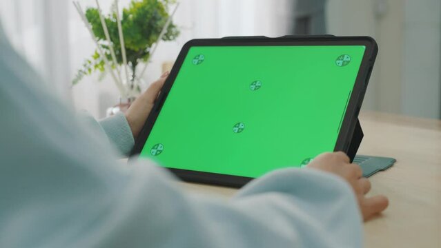 A woman uses a mobile phone or tablet with a green screen to watch videos, surf social media, or have an online conference.