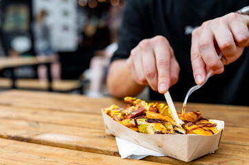 close-up a hand holding a white plastic fork with a piece of grilled food, possibly squid or...