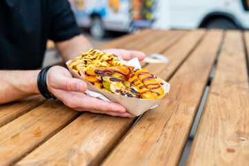 close-up a hand holding a white plastic fork with a piece of grilled food, possibly squid or...