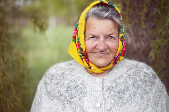 Close up portrait of a senior woman wearing a yellow headscarf in a garden. 