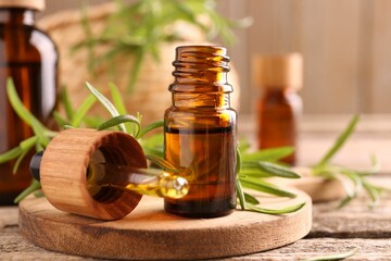 Aromatic essential oil in bottle, pipette and rosemary on wooden table, closeup