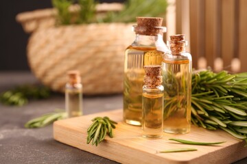 Essential oil in bottles and rosemary on grey table, space for text