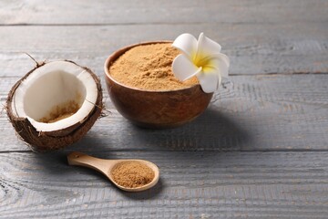 Coconut sugar, bowl, spoon, flower and fruit on grey wooden table. Space for text