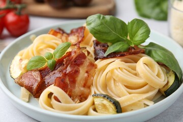 Tasty pasta with bacon and basil on light grey table, closeup