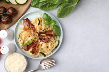 Tasty pasta with bacon and basil on light grey table, flat lay. Space for text