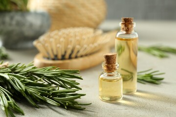 Essential oil in bottles and rosemary on light gray table, closeup