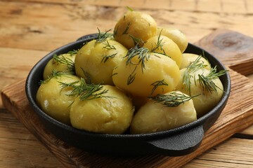 Tasty young boiled potatoes with dill in bowl on wooden table
