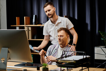 Two men in casual attire working together on a computer in an office setting.