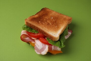 Tasty sandwich with bacon and tomato on green table